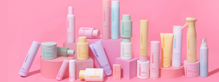 Full range of DESIGNME hair products arranged on pink blocks against a pink background.