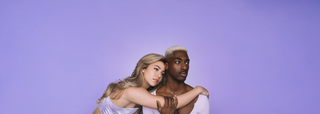 A blonde hair woman and man posing closely against a purple background.