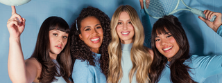 Four smiling women with diverse hair textures and styles, posing together against a blue background.