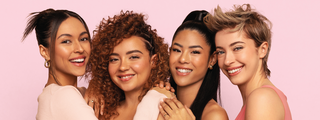Four smiling women with diverse hair textures and styles, sleek updo, curly, long straight, and pixie, posing together.