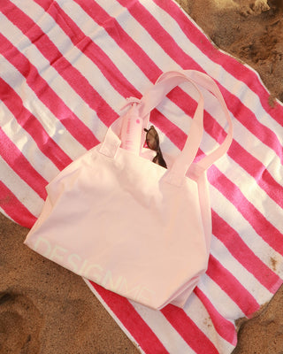 Limited edition tote bag laying on a beach towel with PUFF.ME sea salt spray.